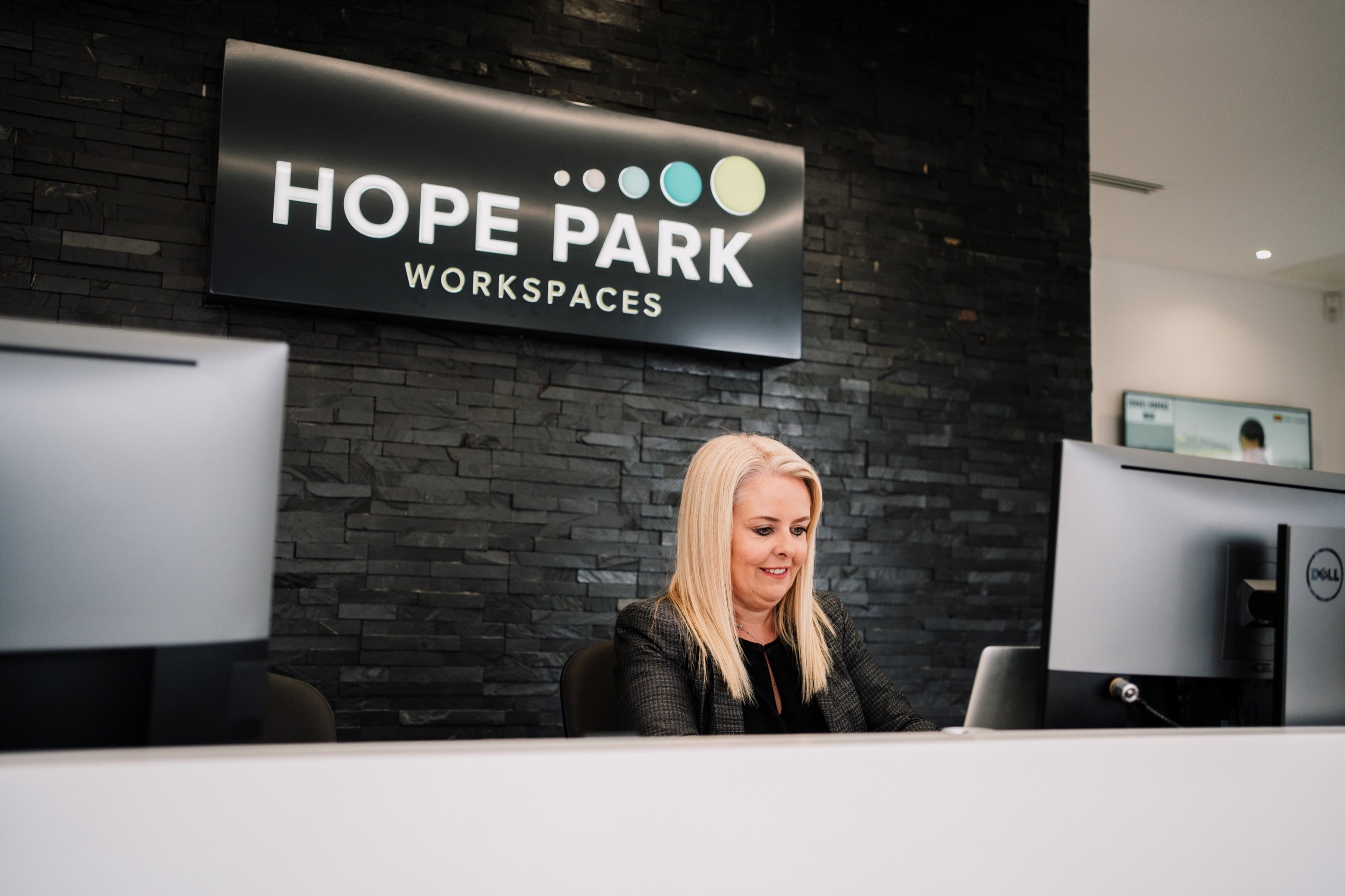 A Hope Park receptionist working at a polished reception desk in front of the Hope Park Workspaces sign